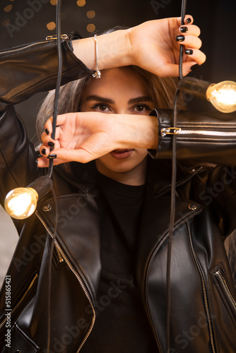 Portrait of a beautiful young model in black leather jacket posing near lamps