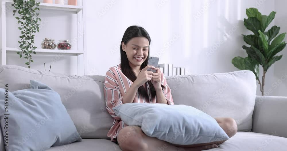 Happy teenage Asian woman playing smartphone on sofa at home, Play games, online shopping. Happy teenage Asian woman playing smartphone on sofa at home, Play games, online shopping.