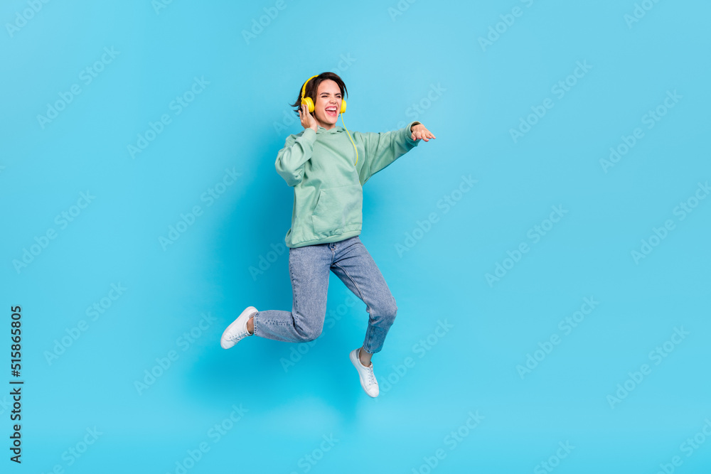 Full body photo of sweet young brunette lady jump wear headphones pullover jeans sneakers isolated on blue background
