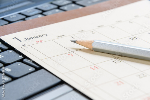 Calendar planner / timetable or schedule arrangement concept : Top view of a silver pencil on a flipped paper / desk calendar. A calendar is a system of organizing days for administrative purposes.