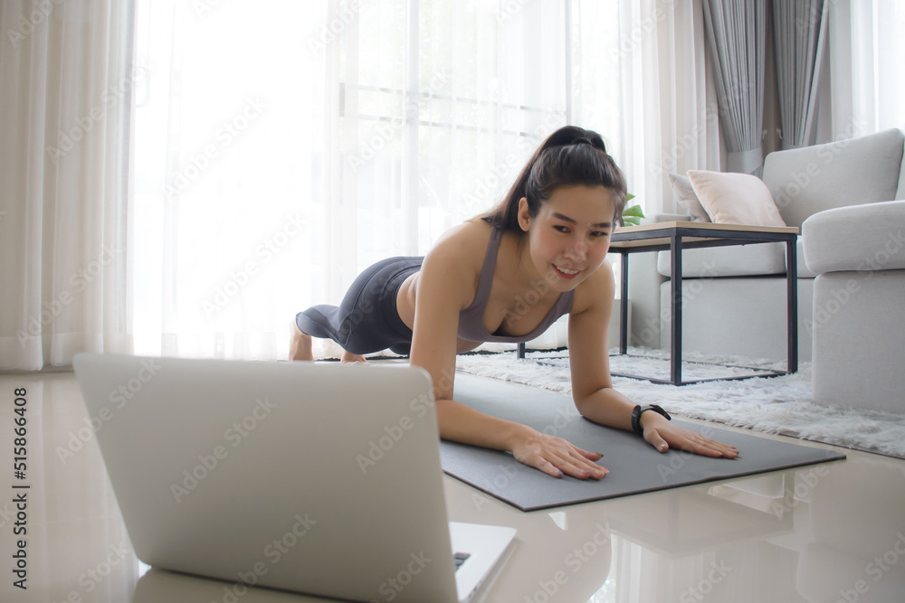 Obraz premium Home workout. Sporty girl exercise on yoga mat in black position workout for core body and abdominal while watching online tutorial via laptop with personal trainer.
