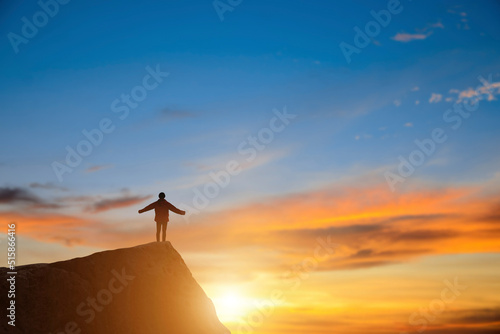 Silhouette of young hikers standing on the rock on top of the mountain mountains with rising hands at sunrise and beautiful sky background.