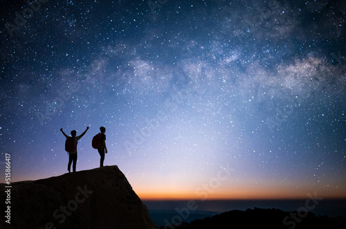 Silhouette of two young man standing  open arms and watched the star  milky way and night sky on top of the mountain. They enjoyed traveling and was successful when he reached the summit.