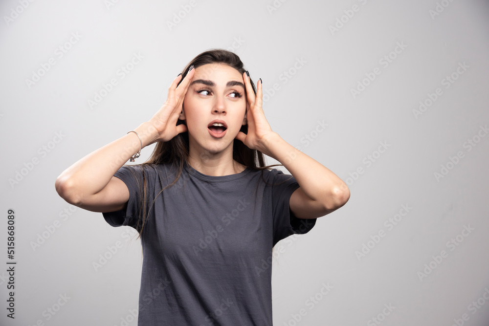 Young woman standing and touching her head over a gray background Young woman standing and touching her head over a gray background