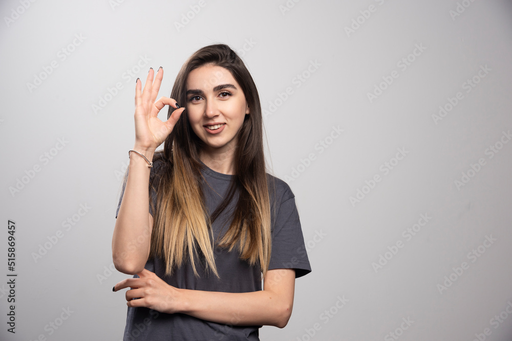 Young woman showing ok gesture and standing over a gray background Young woman showing ok gesture and standing over a gray background