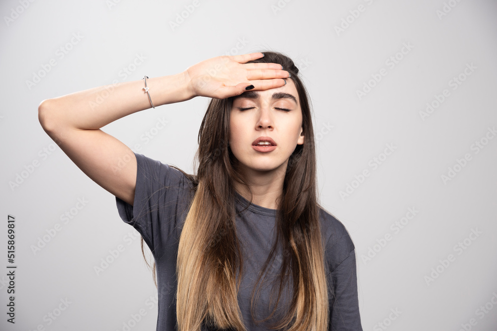 Fototapeta premium Portrait of young woman touching her forehead posing over gray background