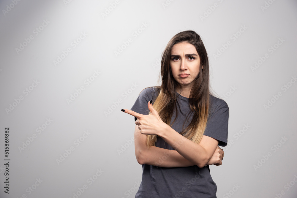Portrait of woman standing and pointing at somewhere over a gray background Portrait of woman standing and pointing at somewhere over a gray background