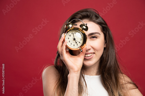 Young woman holding an alarm clock on a red background