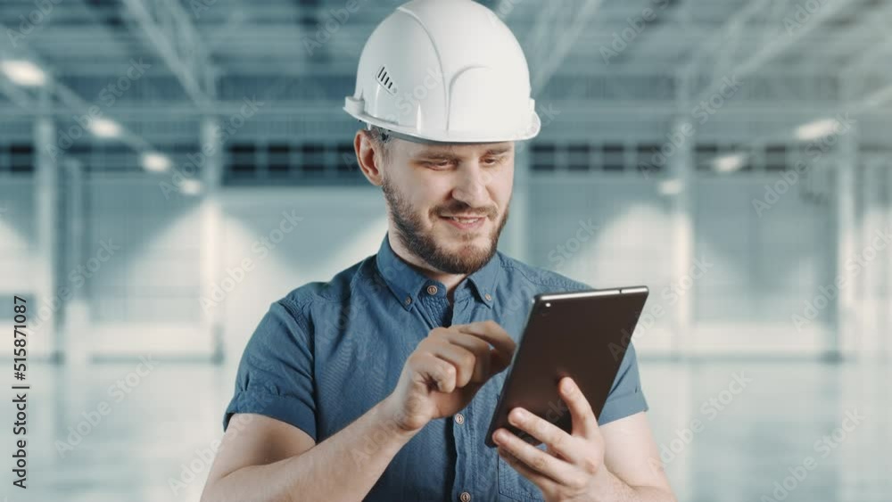 A man construction worker with helmet is smiling and using tablet at building site. Engineer is typing message on gadget and chatting in application. Concept of rest and work or construction. A man construction worker with helmet is smiling and using tablet at building site. Engineer is typing message on gadget and chatting in application. Concept of rest and work or construction.