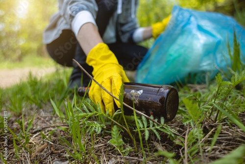 A woman picks up an abandoned glass bottle in the forest. Environmental garbage pollution