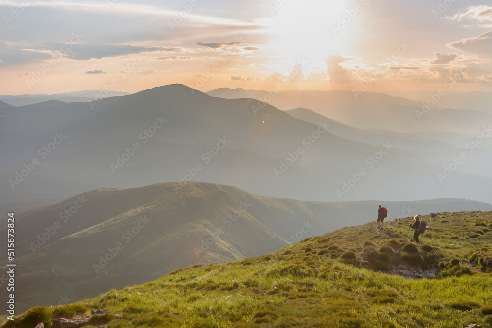 Two hikers tourist in the stoned mountains hills during sunset with orange sky and clouds in the Carpathians, Chornohora