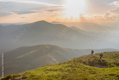 Two hikers tourist in the stoned mountains hills during sunset with orange sky and clouds in the Carpathians, Chornohora