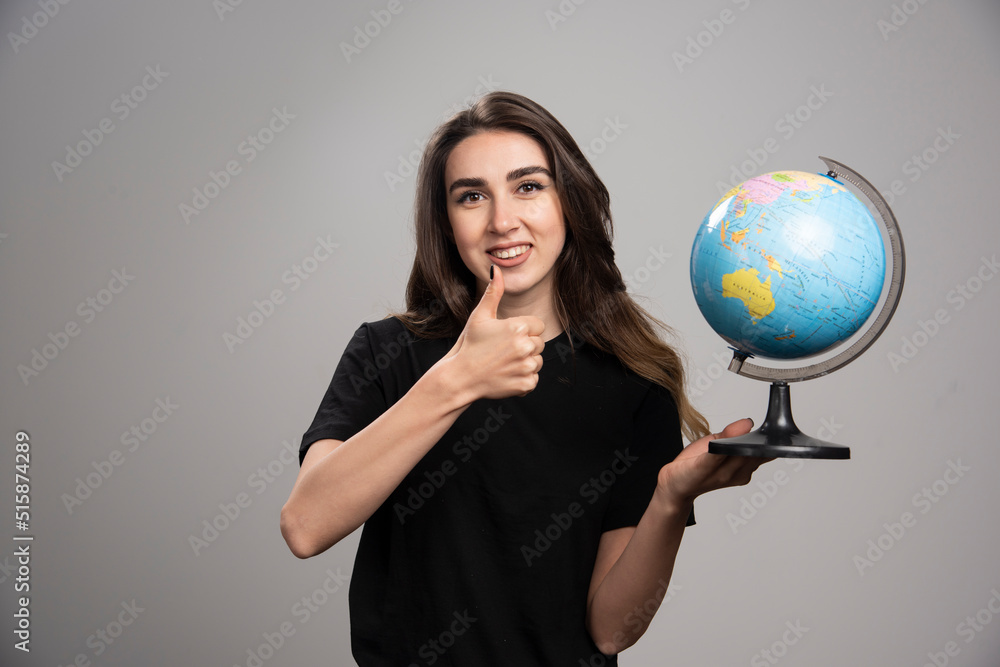 Happy woman with globe making thumbs up on gray background Happy woman with globe making thumbs up on gray background
