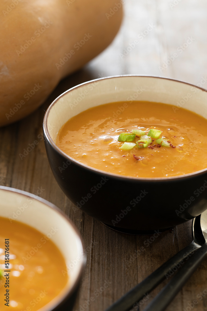 Side view of bowl with delicious pumpkin soup, ingredient like pumpkin and spoons on a wooden table Side view of bowl with delicious pumpkin soup, ingredient like pumpkin and spoons on a wooden table