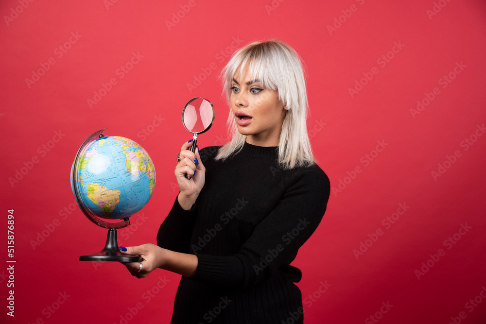 Young woman looking on a globe with loupe on a red background Young woman looking on a globe with loupe on a red background