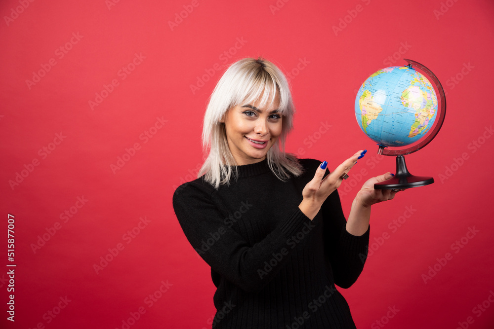 Young woman showing a globe on a red background