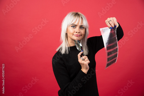 Young woman posing with a loupe and a photo tape on a red background