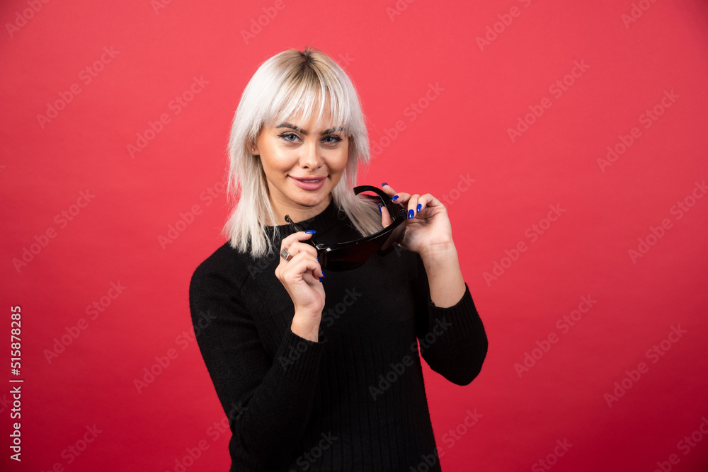 Portrait of woman taking off a black glasses on a red background Portrait of woman taking off a black glasses on a red background