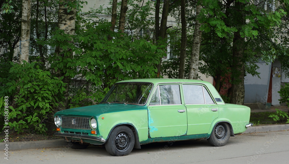 Old green Soviet car in the courtyard of a residential building, Dybenko Street, St. Petersburg, Russia, July 2022