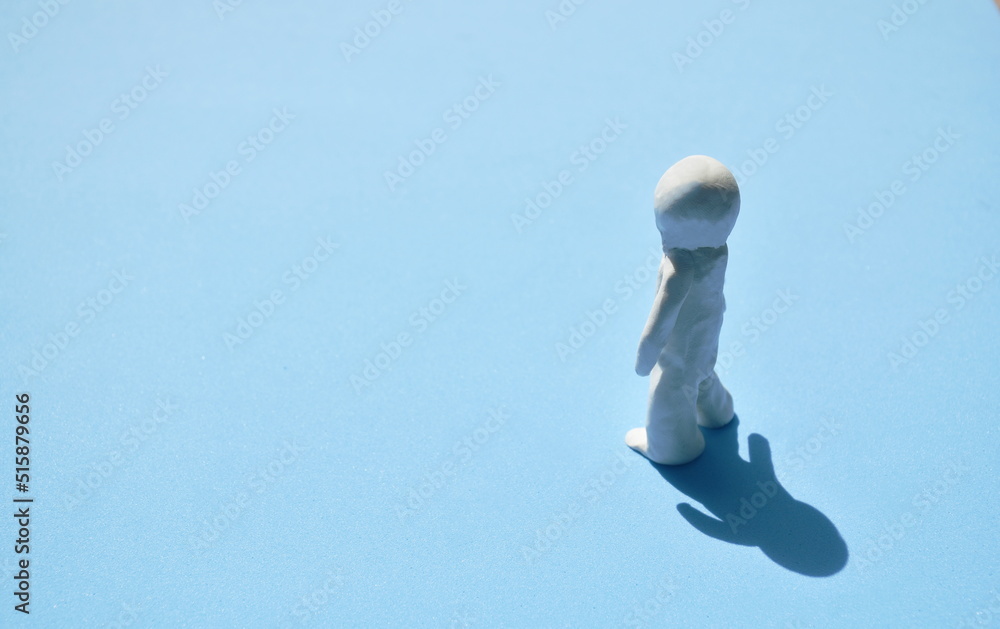 white clay man standing on sunlight with shadow on blue background