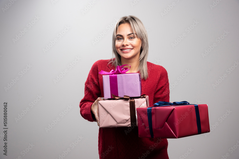 Portrait of cheerful woman offering holiday gifts on gray background Portrait of cheerful woman offering holiday gifts on gray background