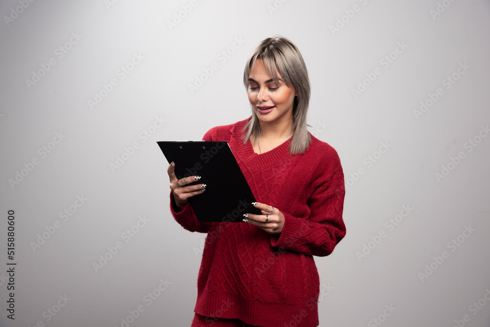 Smiling businesswoman looking at clipboard on gray background Smiling businesswoman looking at clipboard on gray background