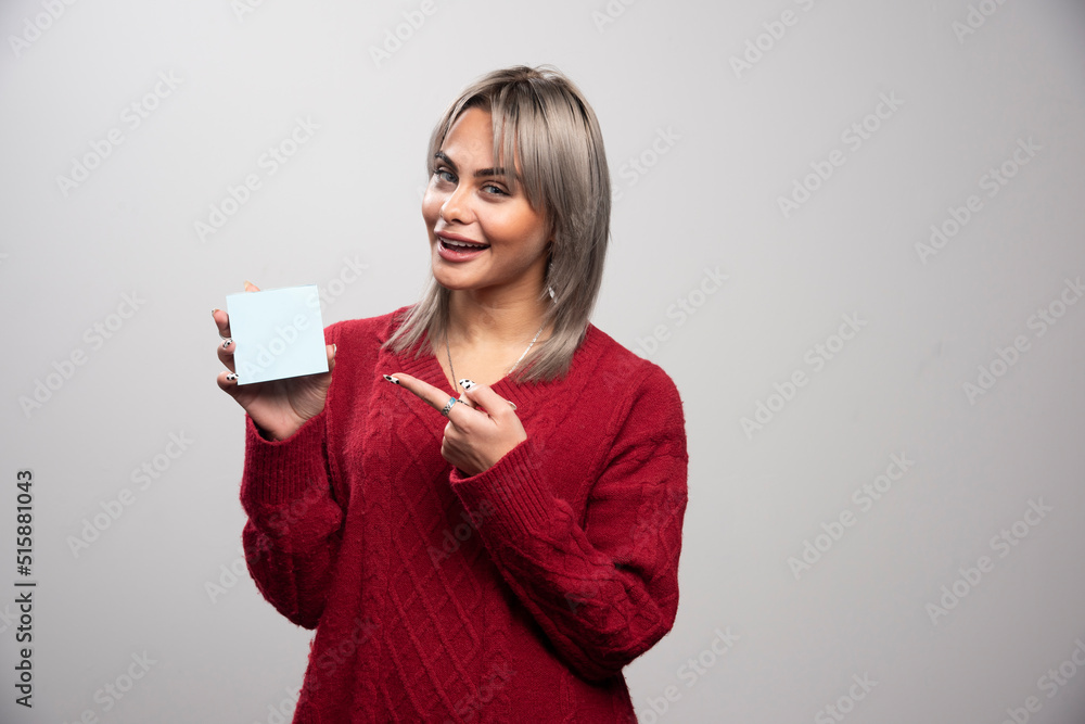 Woman pointing at memo pad on gray background Woman pointing at memo pad on gray background