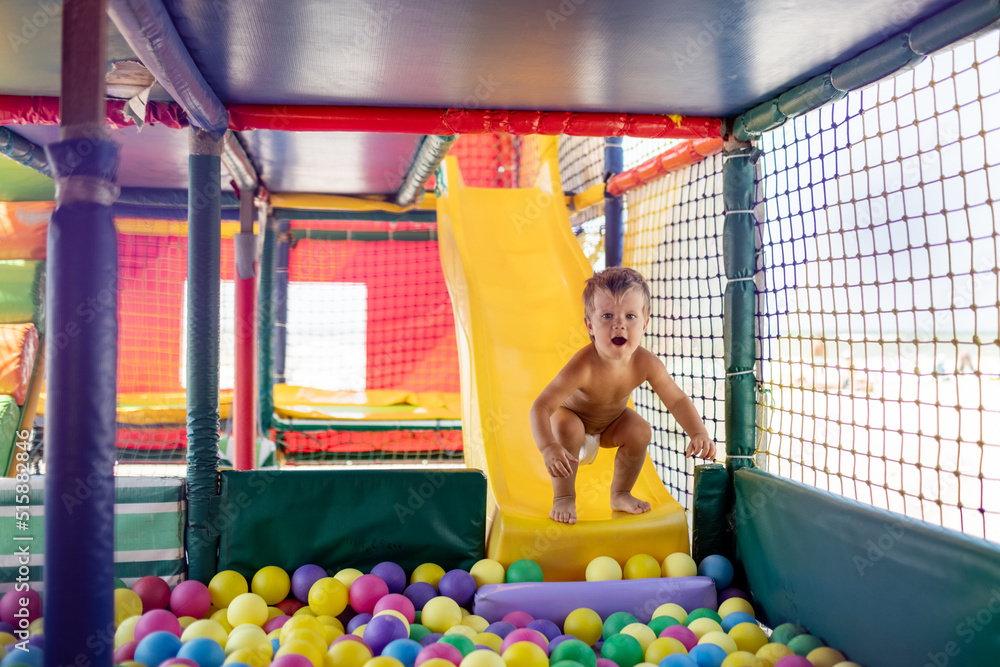 The kid plays in the playroom and rolls down the slide into the pool with small balls The kid plays in the playroom and rolls down the slide into the pool with small balls