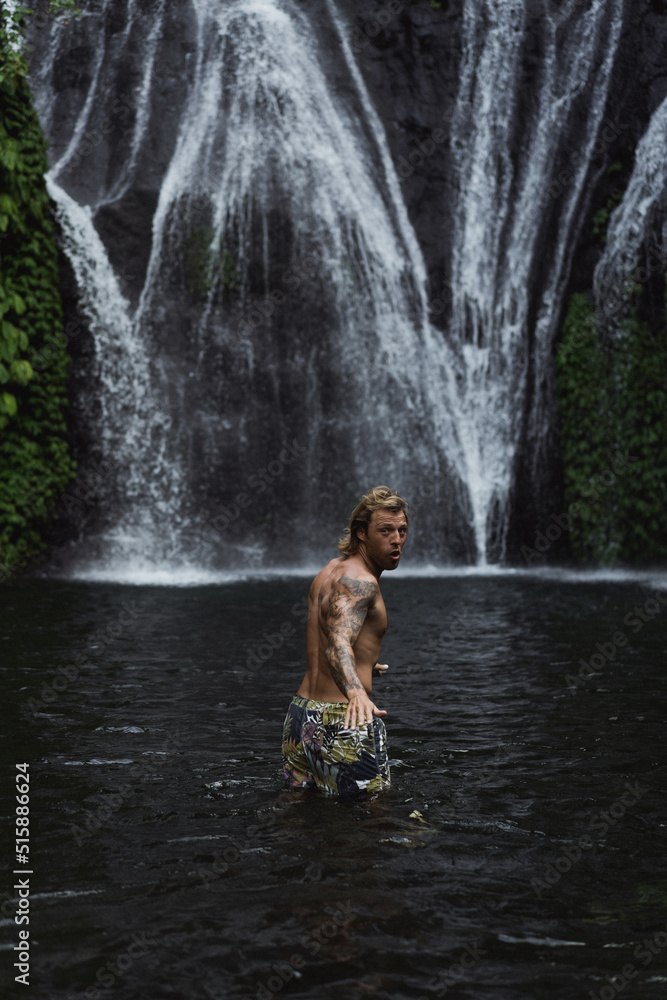 Fototapeta premium Young athletic man swims in a mountain waterfall, Bali landscape, Indonesia. Tourism in Bali.