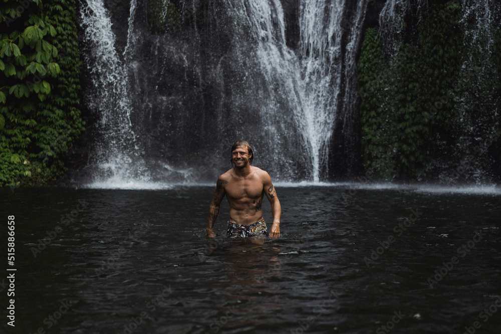 Fototapeta premium Young athletic man swims in a mountain waterfall, Bali landscape, Indonesia. Tourism in Bali.