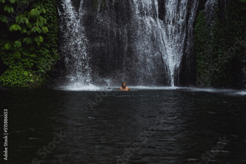 Young athletic man swims in a mountain waterfall  Bali landscape  Indonesia. Tourism in Bali.