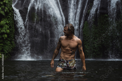 Young athletic man swims in a mountain waterfall  Bali landscape  Indonesia. Tourism in Bali.