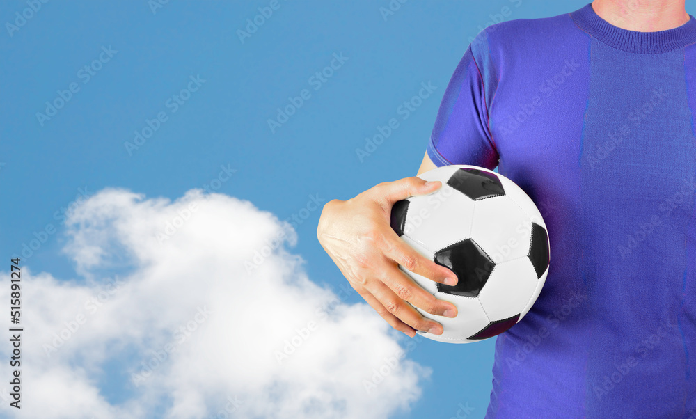 Cropped image of a young man holding a soccer ball with his hand wearing blue tshirt over isolated cloud background with copy space.Online cloud communication concept