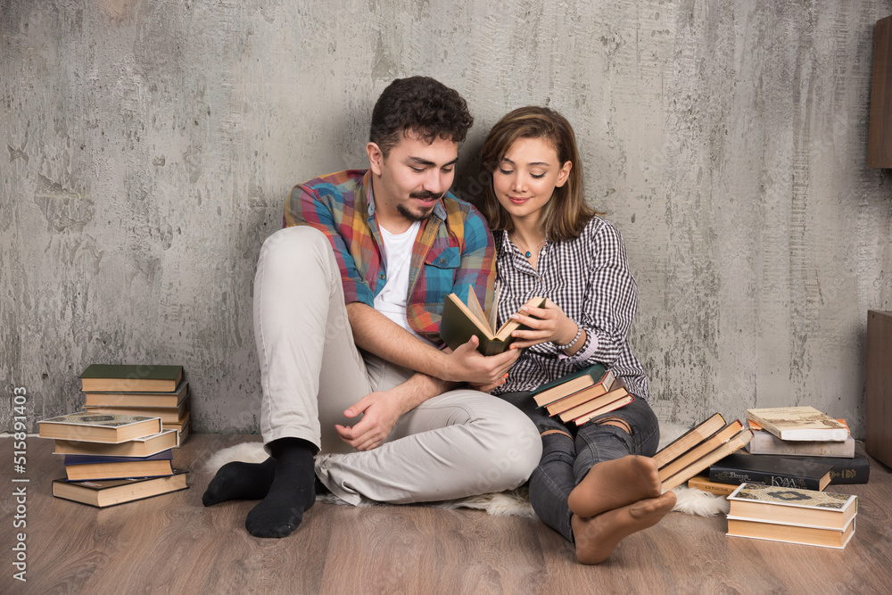 Obraz premium Photo of young couple sitting on the floor and reading a book