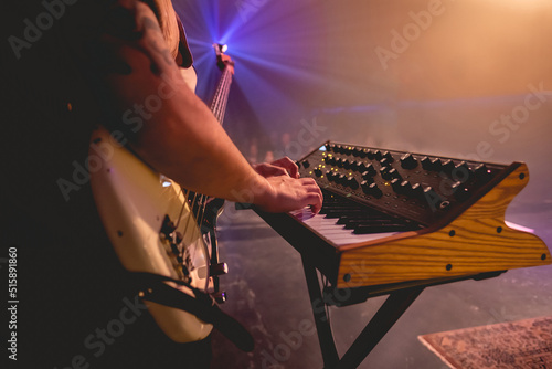 Closeup of young latino bassist and keyboardist with shirt, and cream bass and vintage keyboard playing live in a concert under colorful lights photo