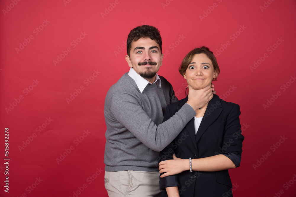 Young man playfully strangles woman on red background Young man playfully strangles woman on red background