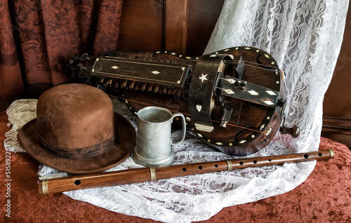 An antique musical instrument called a Hurdy-Gurdy with a bowler hat and tin mug and flute