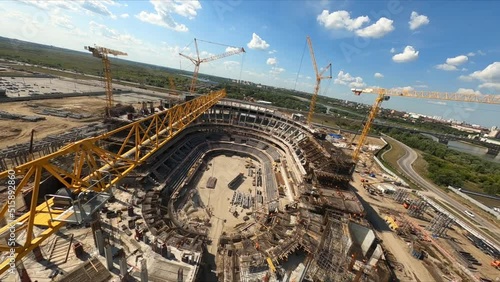 Assembling sports stadium with high cranes and professional workers at construction site in city on sunny day first point view photo