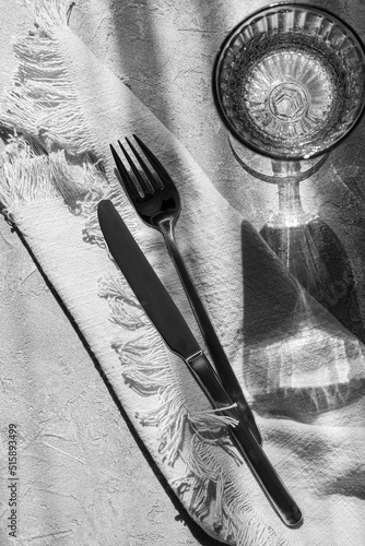Table setting- cutlery, napkin and glass of drink  with strong shadows on the table. Minimal home decor. Black and white photography.