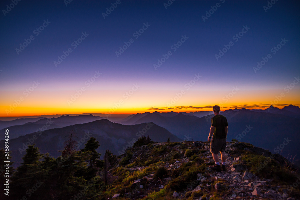An athletic adventurous male hiker standing on top of a mountain looking out at a beautiful sunset.