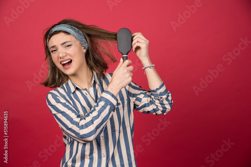 Young girl combs her tangled hair on red background