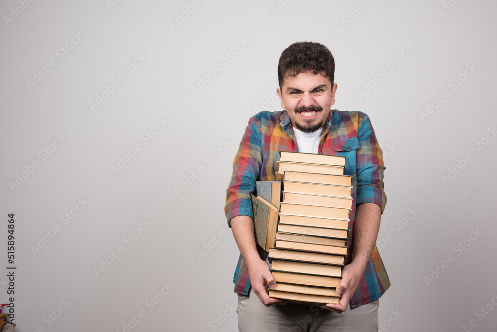 Exhausted male student holding bunch of heavy books Exhausted male student holding bunch of heavy books