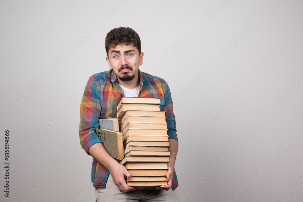 Exhausted male student trying to hold bunch of heavy books Exhausted male student trying to hold bunch of heavy books
