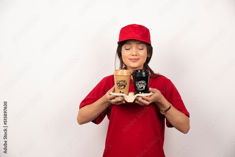 Young woman courier sniffs aroma coffee for delivery on white background