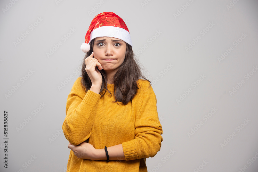 Young woman in Santa Claus red hat posing over a white wall Young woman in Santa Claus red hat posing over a white wall