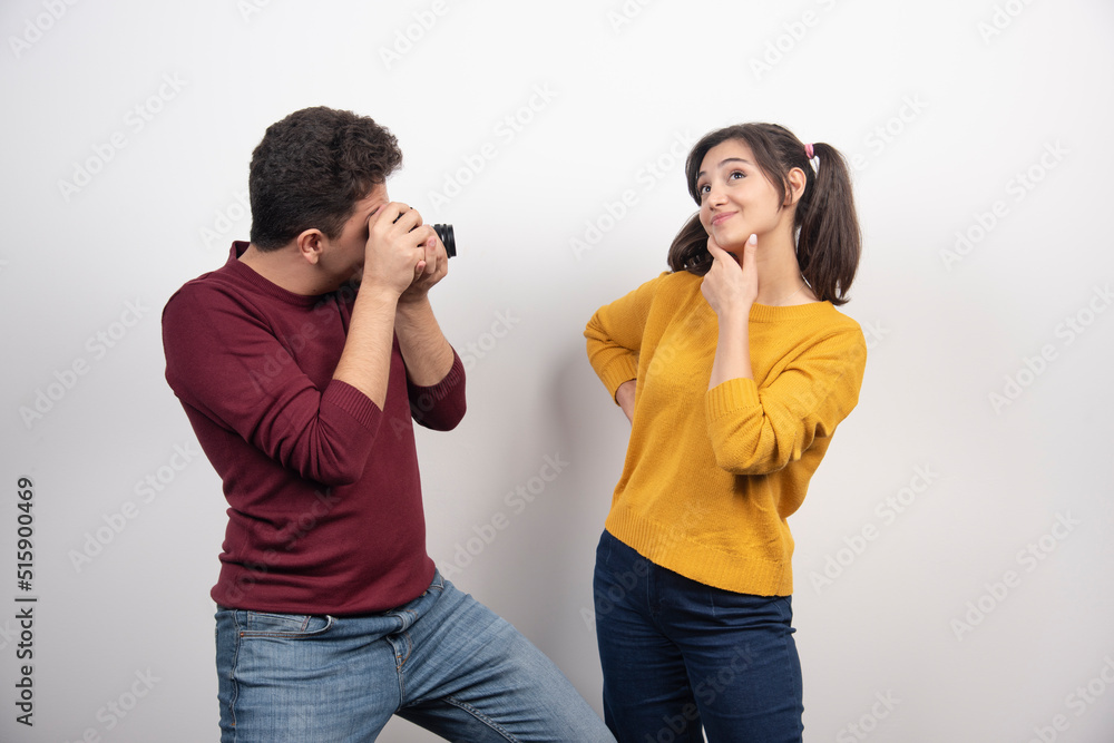 Cute couple taking pictures with camera and posing over a white wall Cute couple taking pictures with camera and posing over a white wall