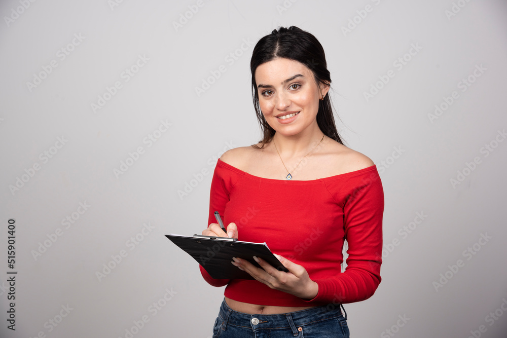 Smiling woman writing in a clipboard and looking at the camera Smiling woman writing in a clipboard and looking at the camera