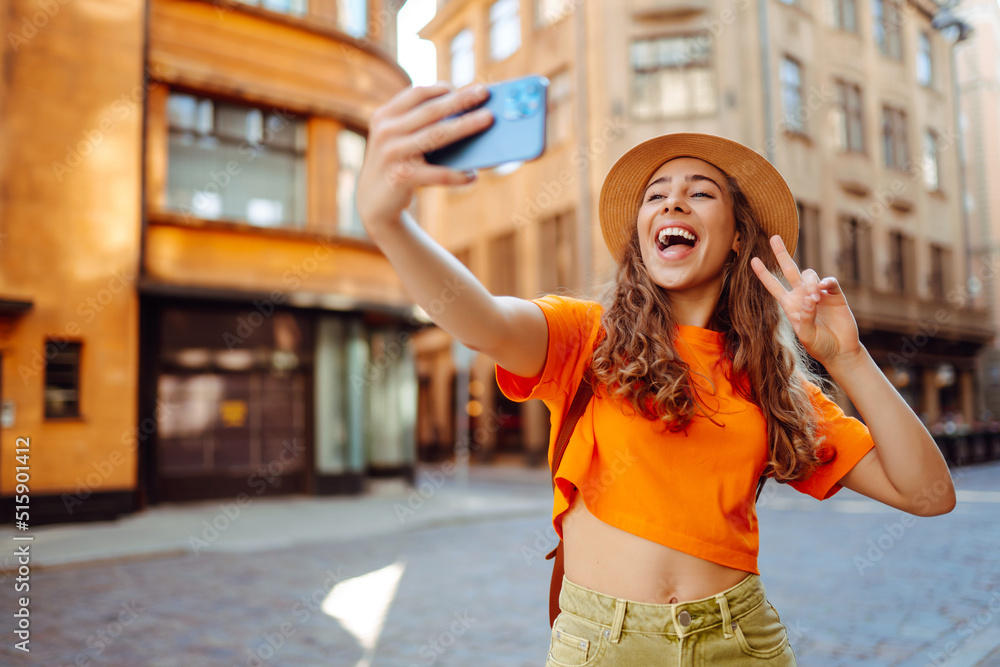 Selfie time. Young woman olding mobile phone taking selfie photo using smartphone camera. Beautiful girl walks through the streets  and takes pictures of some sights .Lifestyle, travel, tourism.