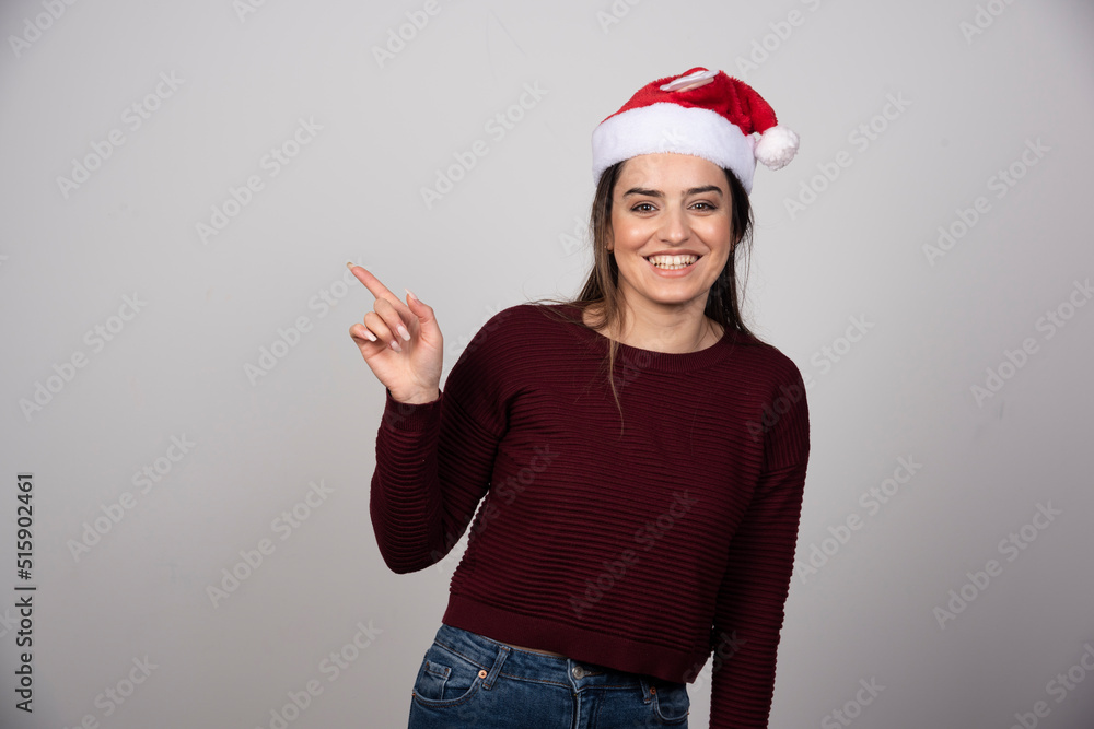 Photo of cheerful woman wearing Christmas hat pointing up