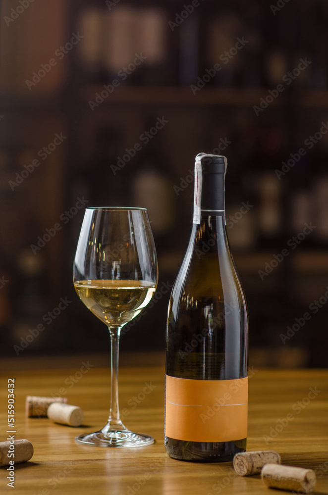 A bottle and a glass of white wine on a wooden table on a wine bar background. Bottle caps on the table